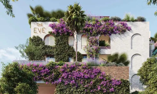 Exterior of The EVE hotel - a white building with arched windows, climbing greenery and purple flowers in bloom